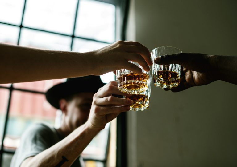 Three people toasting with whiskey glasses in a warmly lit setting