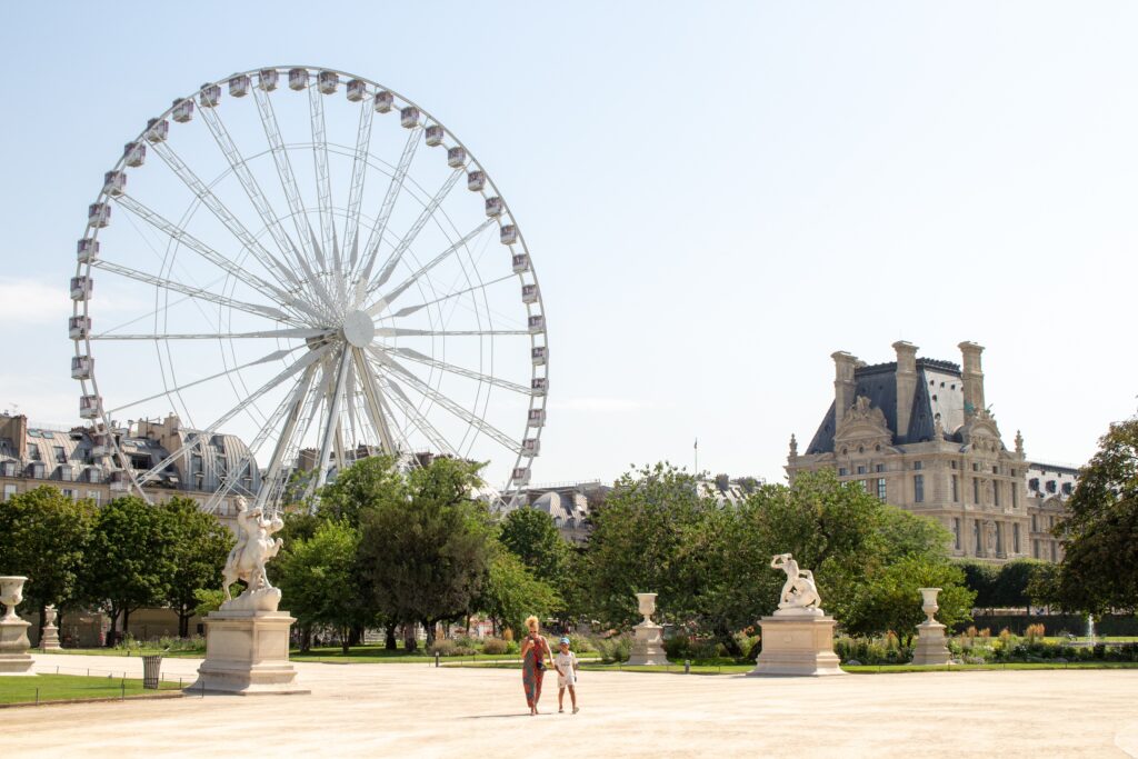 Paris on a budget - a view of the Tuileries gardens, a palace, a woman with a kid, statues, and a ferry wheel