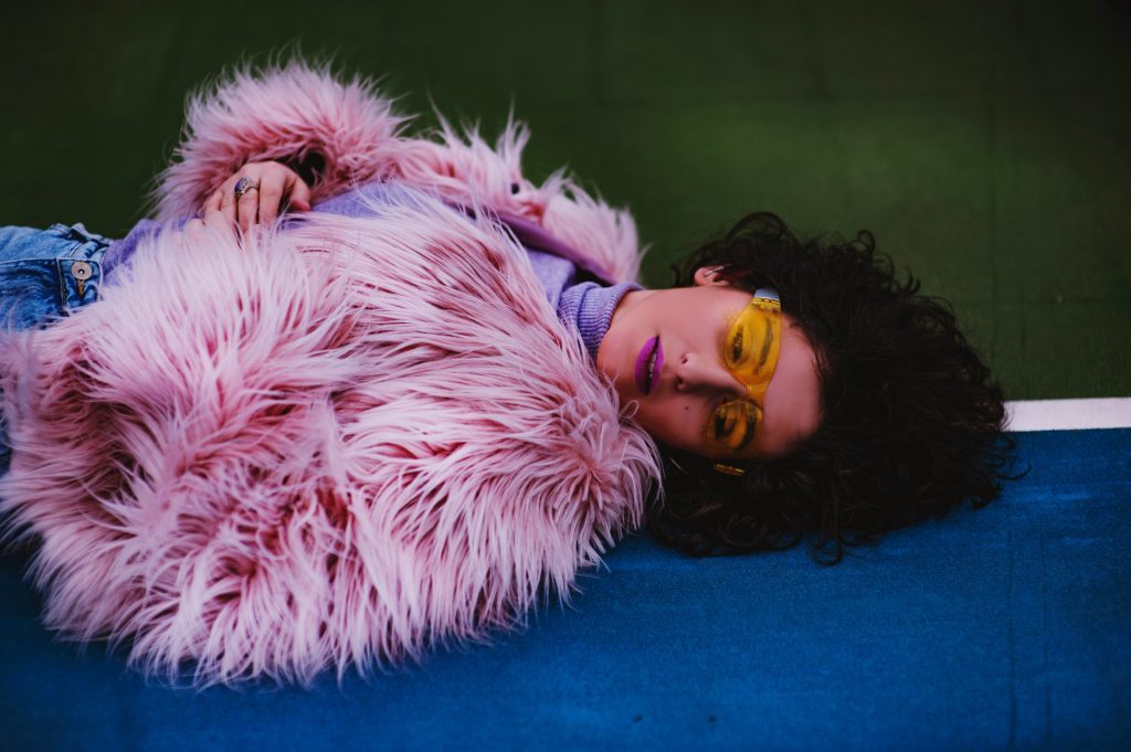 Vintage shops Munich: a girl lying dressed with a pink faux fur and a pair of yellow-framed sun glasses