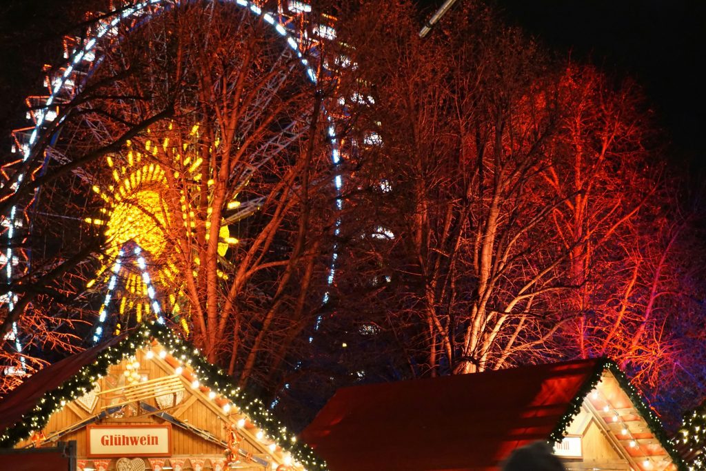 Christmas markets Vienna: a ferris wheel with Christmas lights in the night and the roof of two Christmas stalls