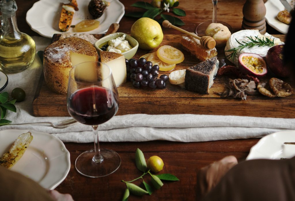 Feiertage in Frankreich: eine Auswahl an Käse und Früchten sowie ein Glas Wein im Vordergrund.