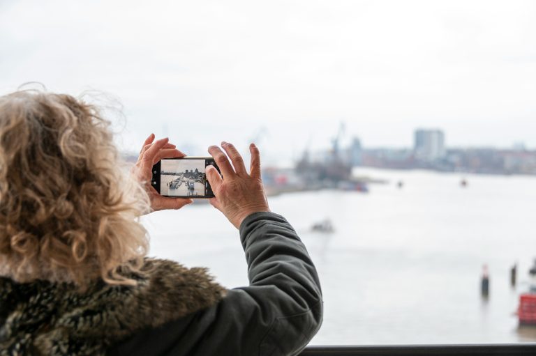 Woman with curly hair taking a photo of a Hamburg harbor view with her smartphone