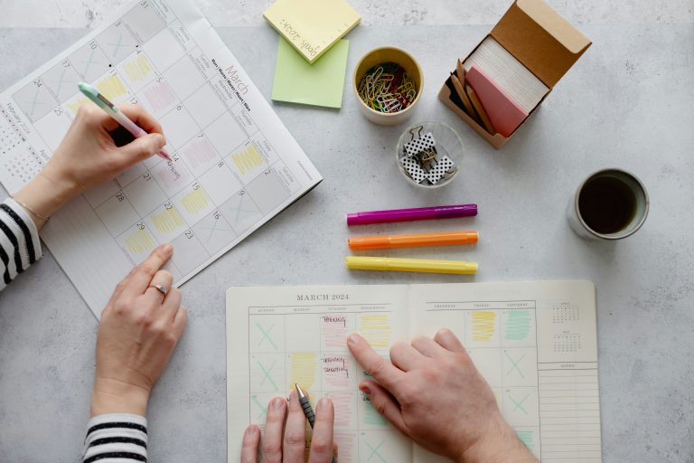 Two people planning a schedule with calendars, markers, and office supplies