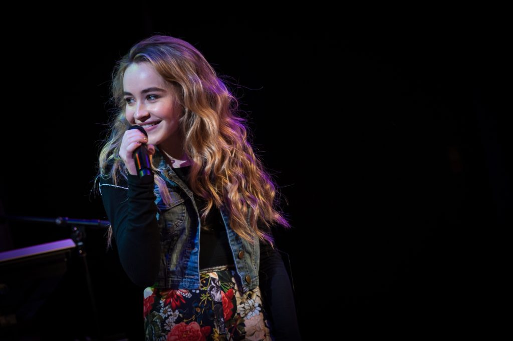 Sabrina Carpenter tour Europe: Sabrina Carpenter smiling while performing on stage, holding a microphone