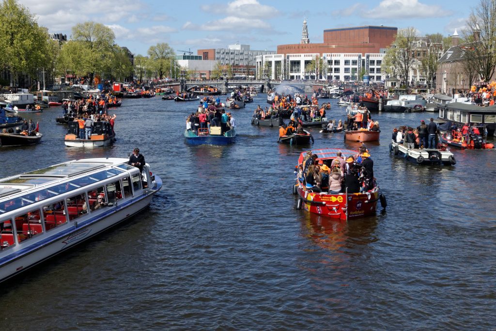 Bank holiday the Netherlands: boats filled with people celebrating King’s Day on Amsterdam canals.