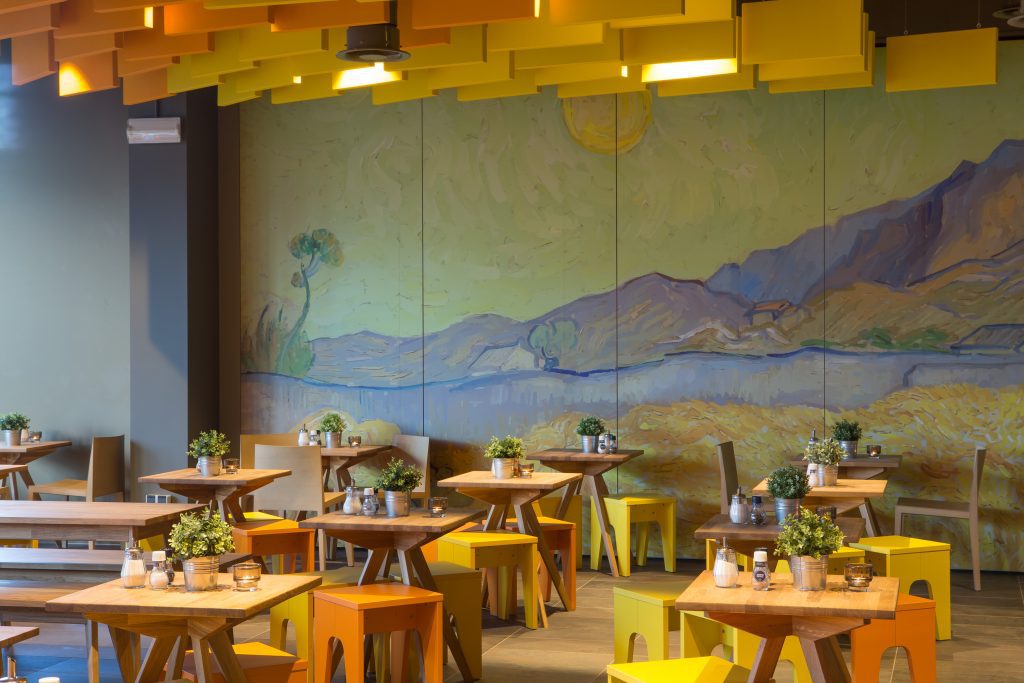 Room with decor wall, yellow deco on the ceiling, wooden tables and yellow seats