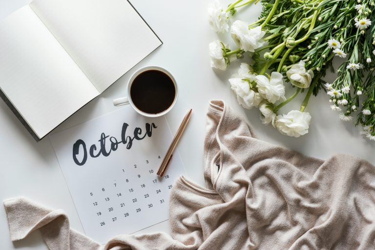 Cozy October setup with a calendar, coffee, flowers, and a soft beige sweater