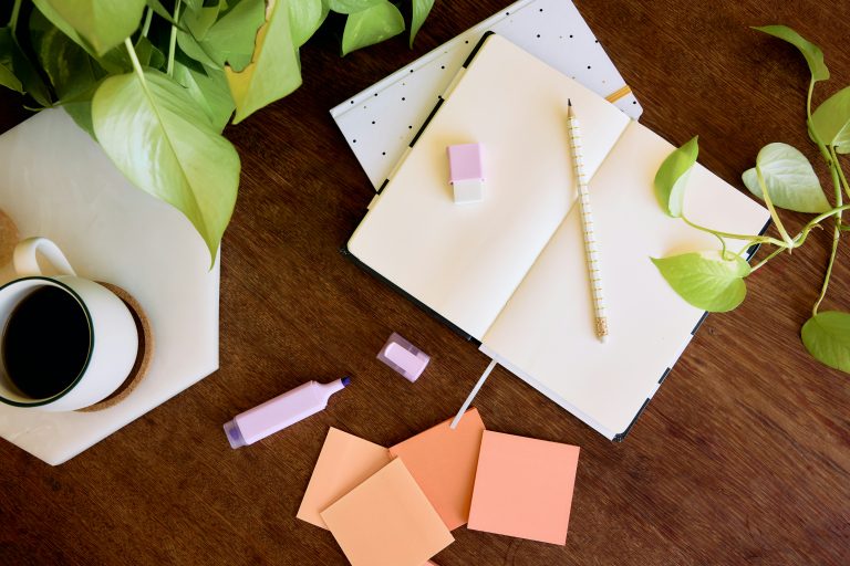 Organized workspace with an open notebook, pencil, sticky notes, and a cup of coffee